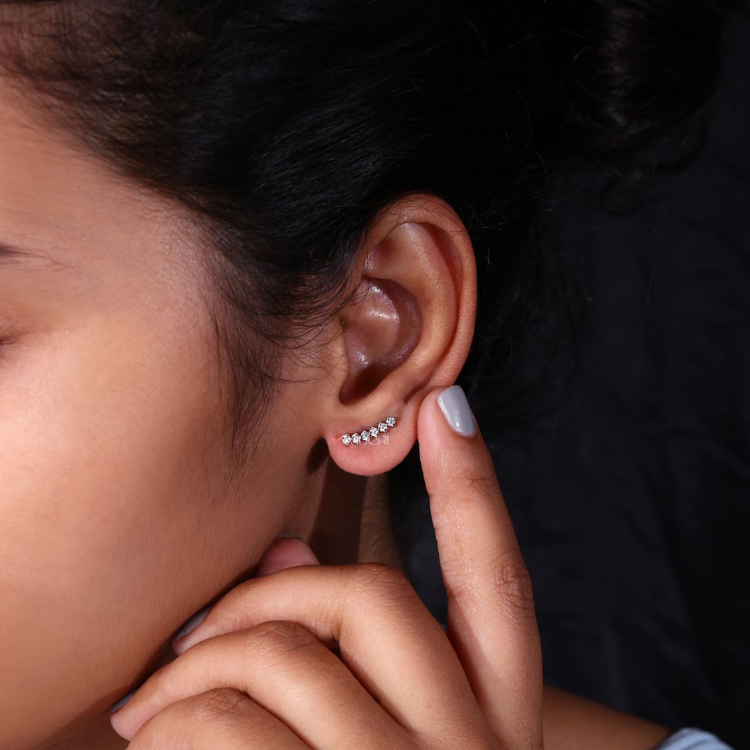 White gold Arc stud earrings resting on a sleek black surface.
