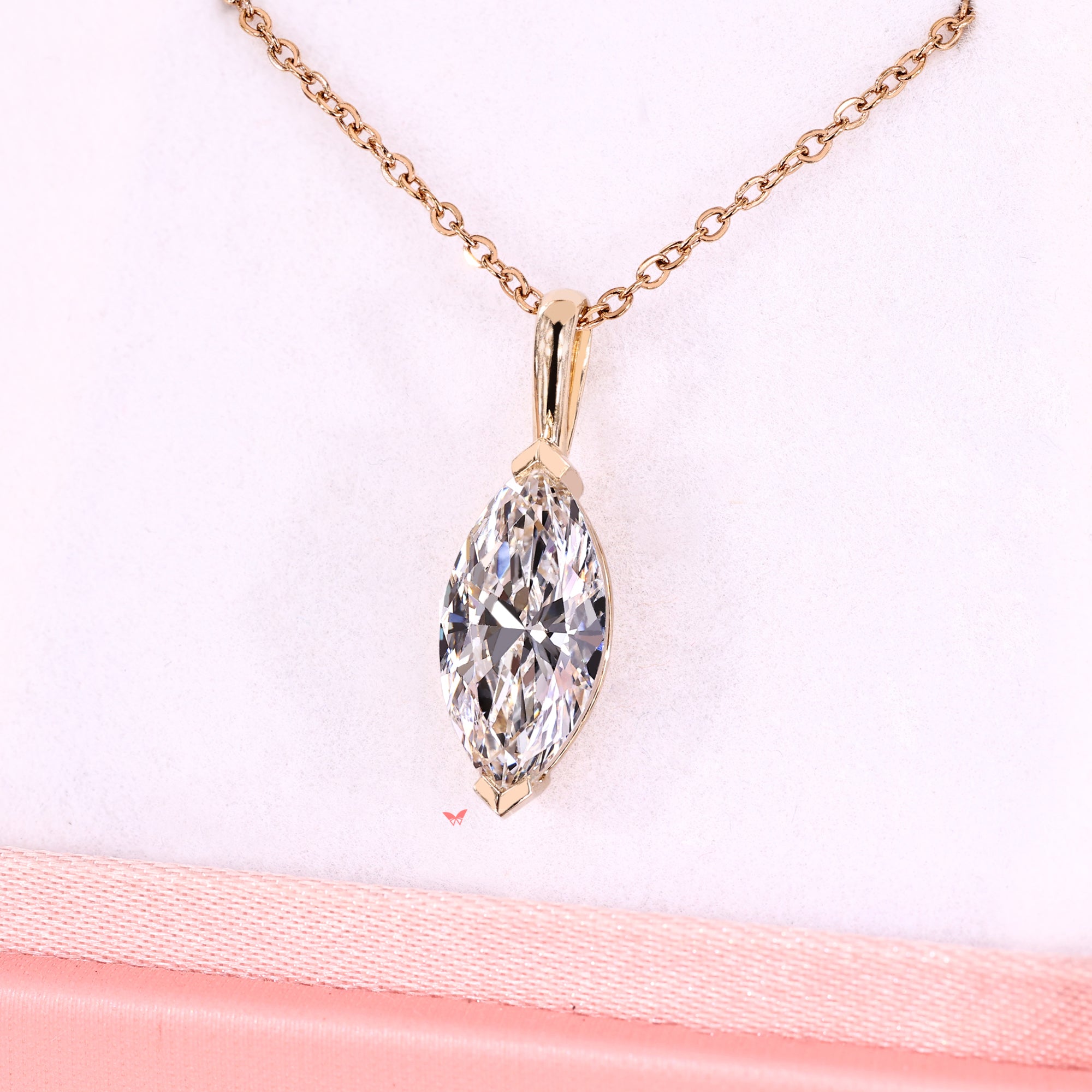 Gold necklace with a marquise-shaped diamond pendant on a light pink background