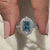 Blue Diamond Ring Held Between Two Finger.