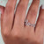 She holds a round cut moissanite ring between her fingers.