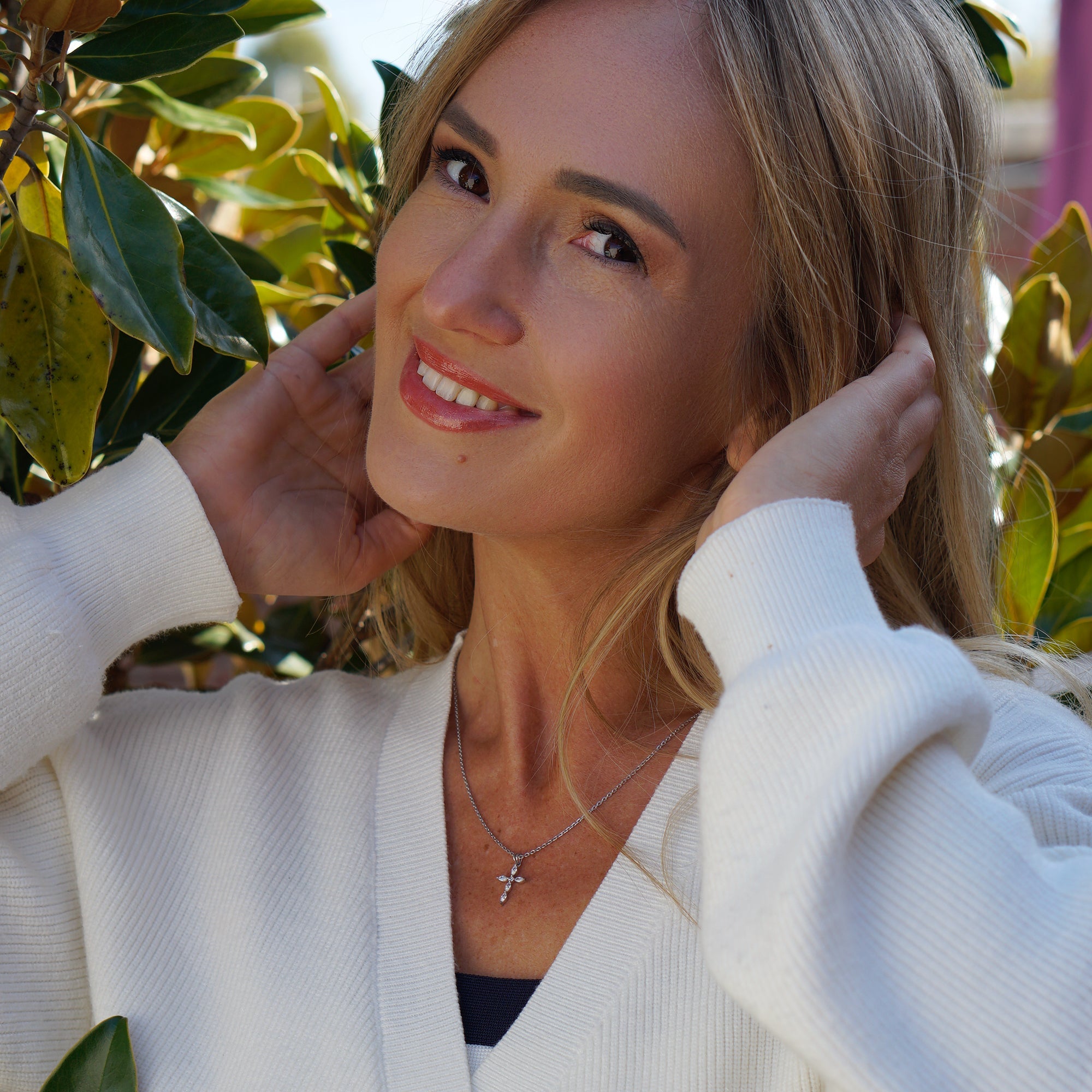 Woman in a white cardigan standing among green foliage