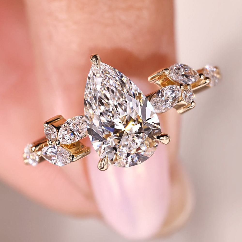 Pear diamond ring with a marquise and round side diamond layout in yellow gold.
