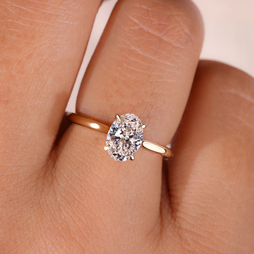 An image of an oval-cut diamond solitaire engagement ring in yellow gold, worn on a hand, showcasing a stunning simplicity design.
