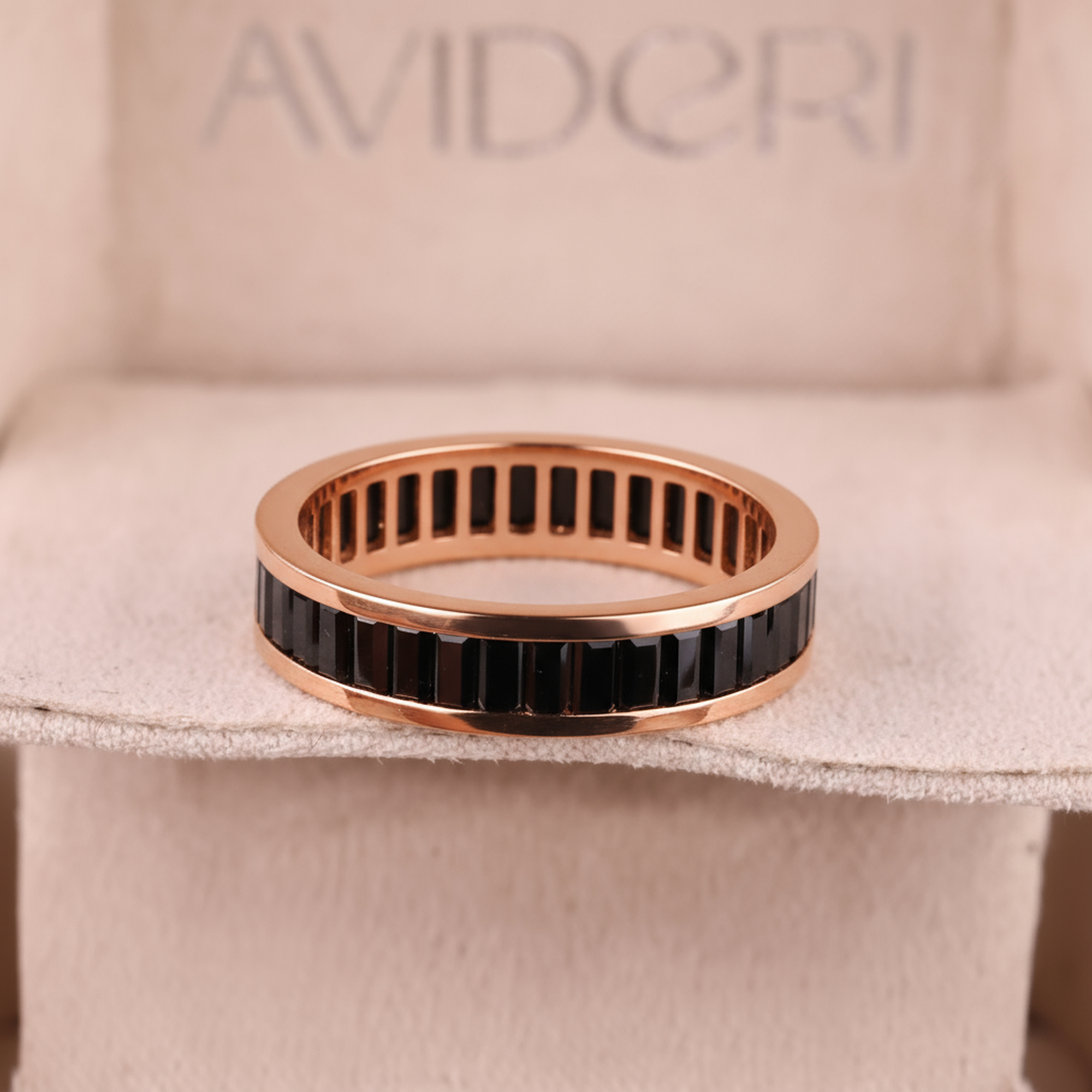 Rose gold ring with black stones on a beige cushion with 'AVIDCRI' branding.