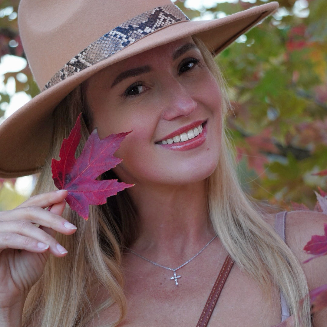Woman wearing a wide-brimmed hat with a decorative band, holding a red leaf, with a blurred natural background.