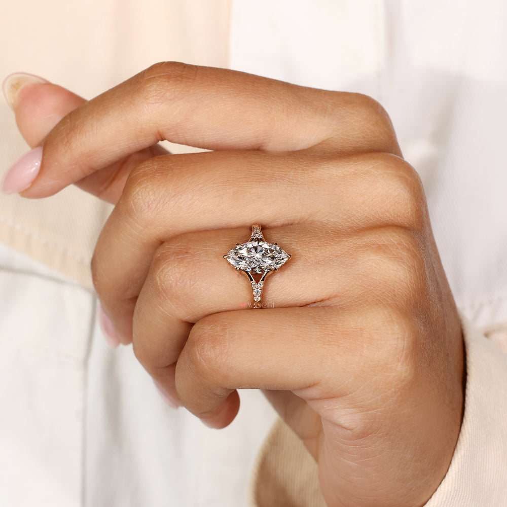 A close-up of a hand wearing a marquise-cut diamond engagement ring with a rose gold setting, shown against a soft cream-colored background.