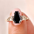 Gold ring with a black gemstone on a finger against a neutral background