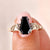 Gold ring with a black gemstone on a finger against a neutral background
