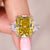 Ring with a yellow gemstone held by a hand against a neutral background