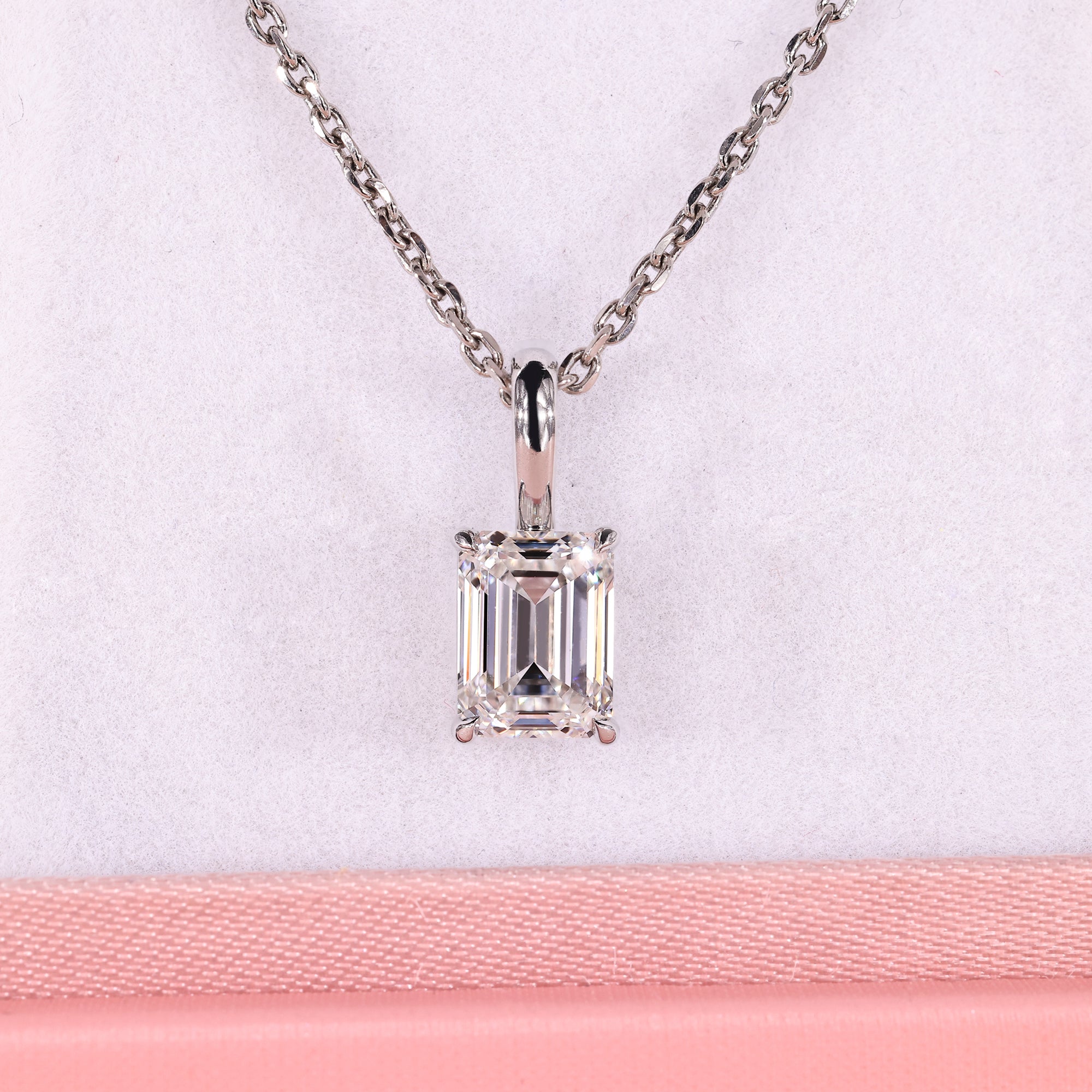 Emerald solitaire pendant in white gold with claw prong setting.
