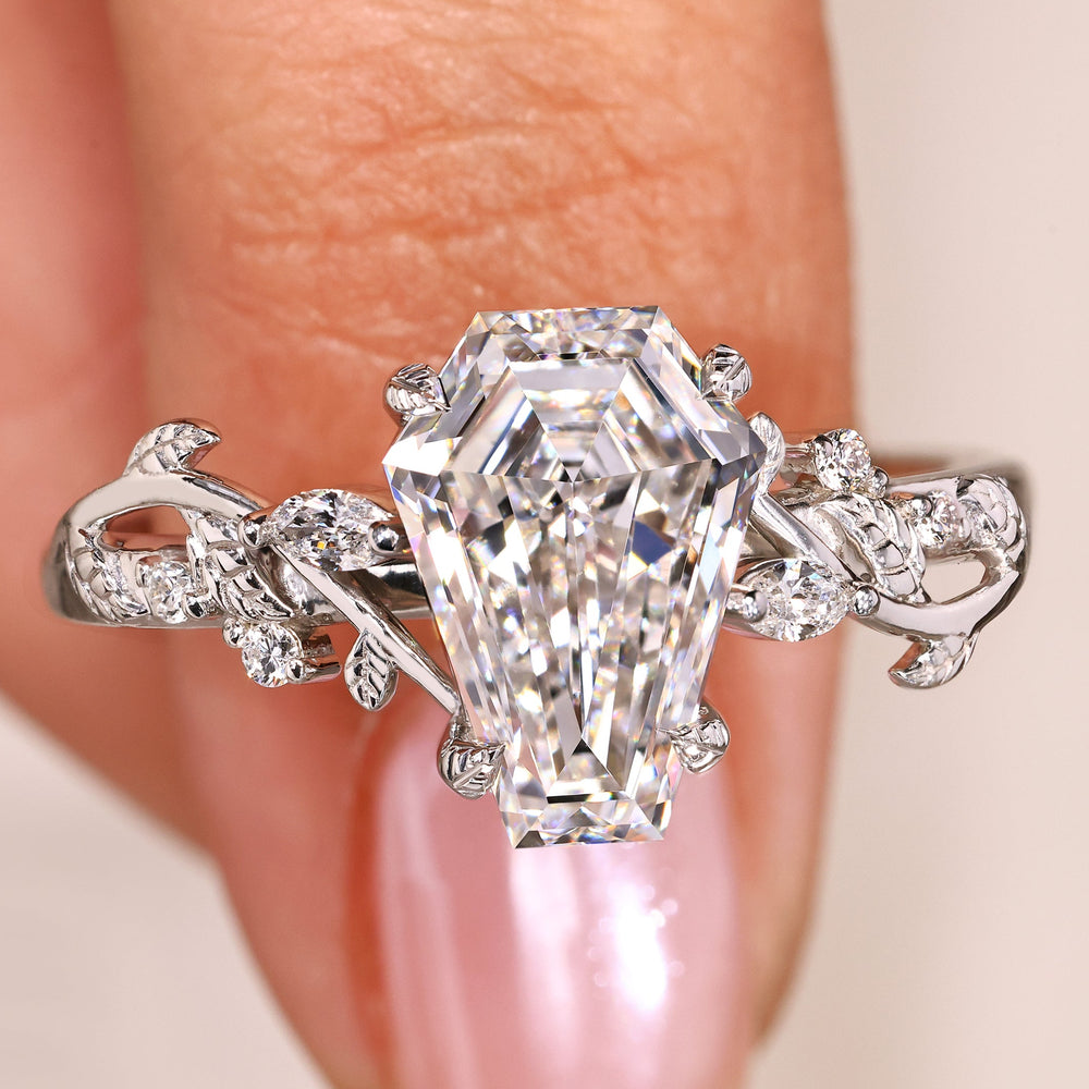 Coffin Diamond ring held by a hand with a soft pink background