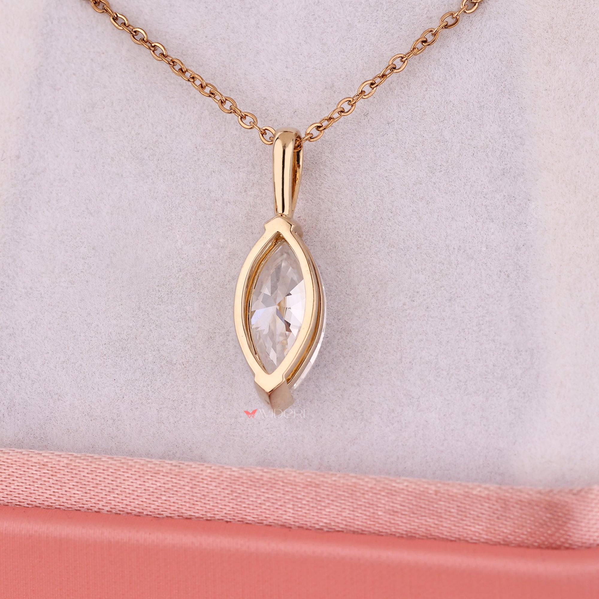 Gold necklace with a marquise-shaped pendant on a light pink background