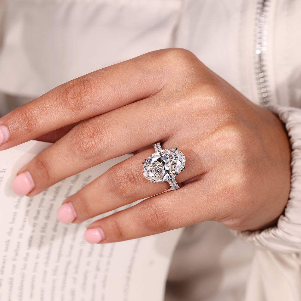 Oval diamond ring with double claw prong setting and pave band.