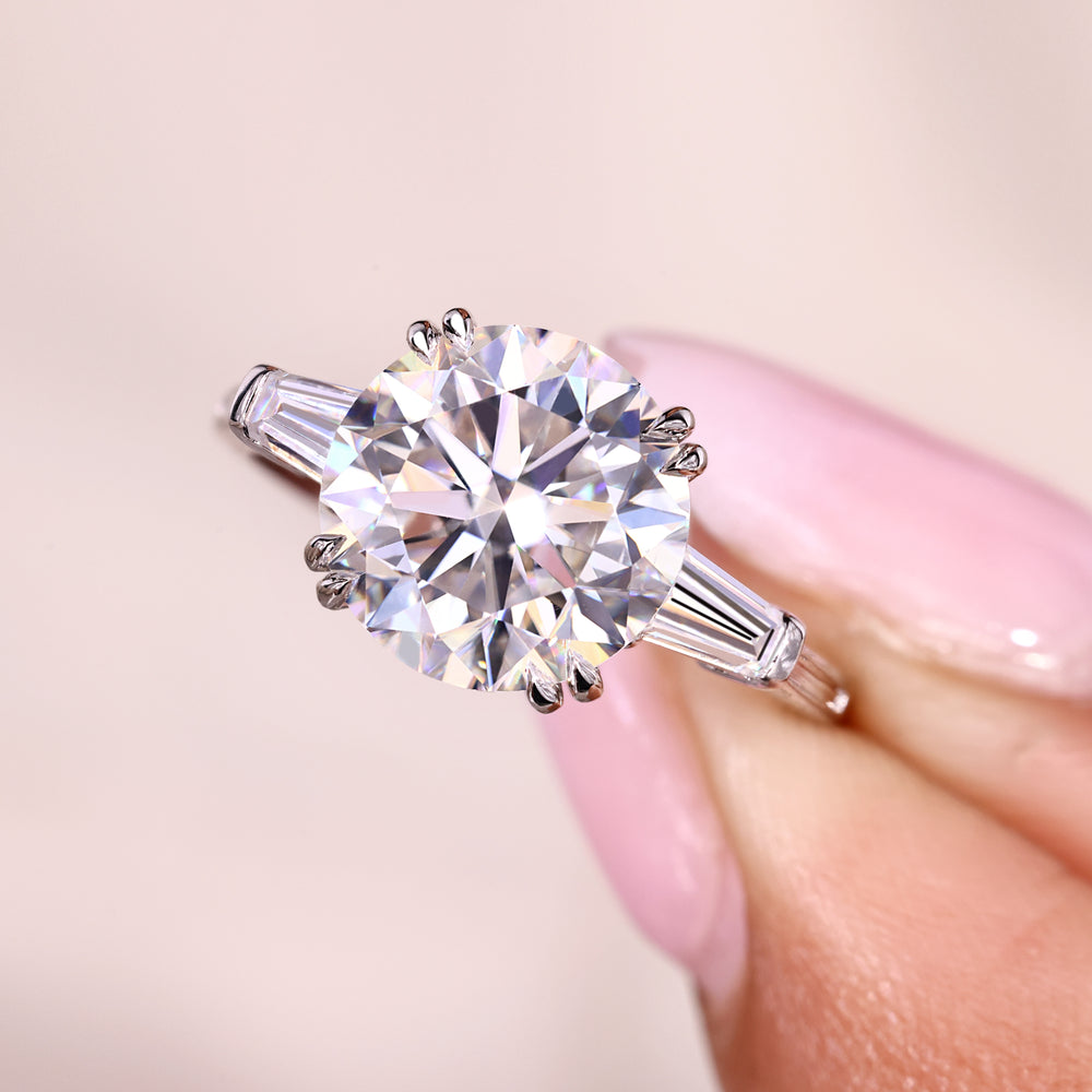 Round moissanite engagement ring with baguette side stones.
