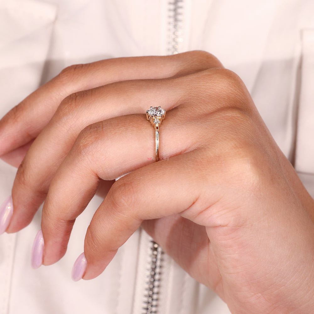 Side view of a yellow gold ring featuring three diamonds and a six prong center setting.