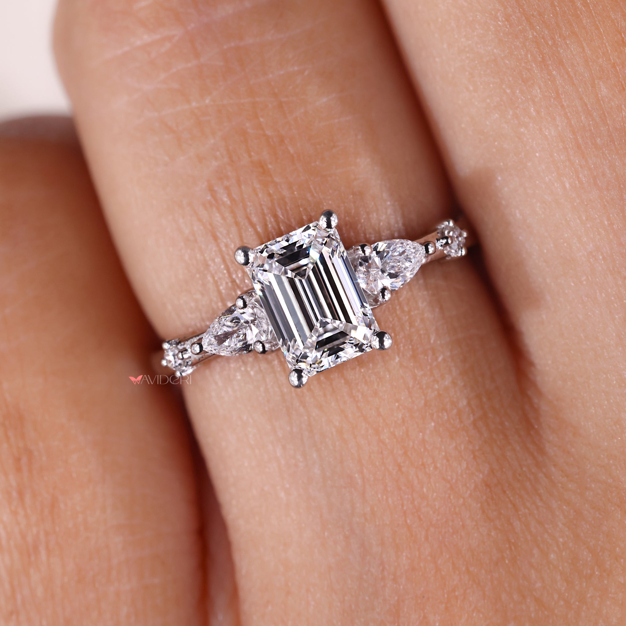 White gold ring created using handmade jewelry with emerald diamond and round side stones.
