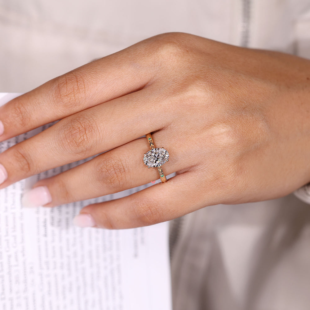 Oval diamond ring with emerald and round side stones.
