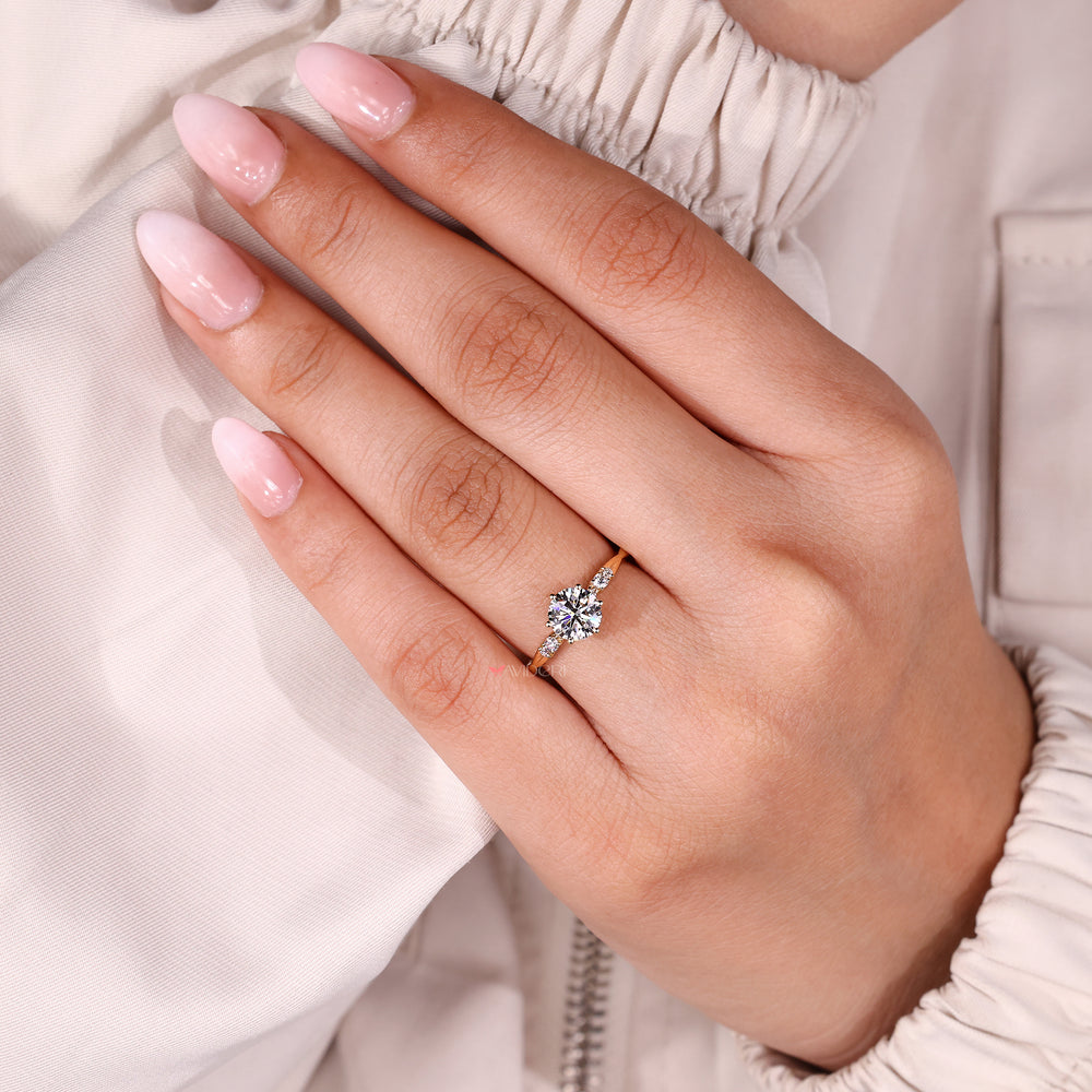 An image of a round diamond engagement ring set with six prongs, featuring a yellow gold band with sparkling side stones.