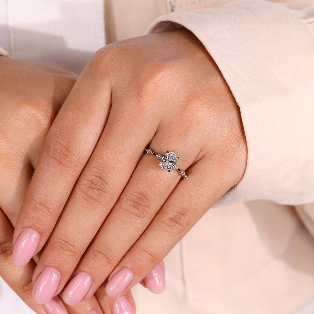 An image of a hand wearing an oval diamond ring with a delicate band and sparkling side stones.