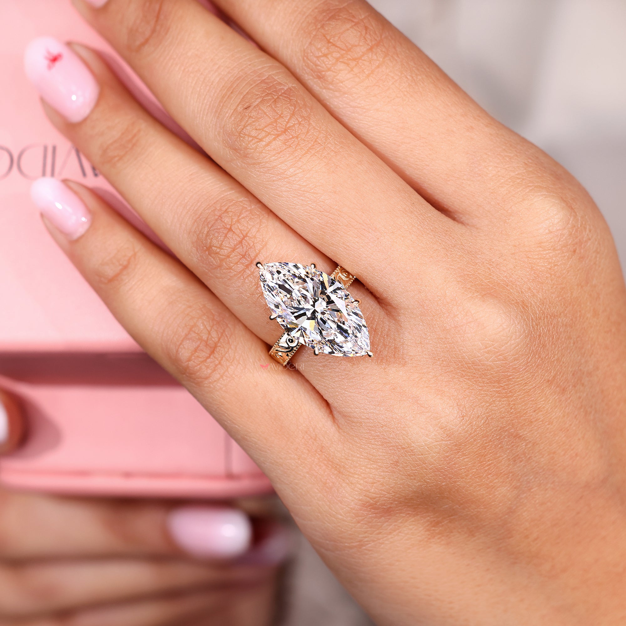 Close-up of a hand wearing a diamond ring with a pink background.