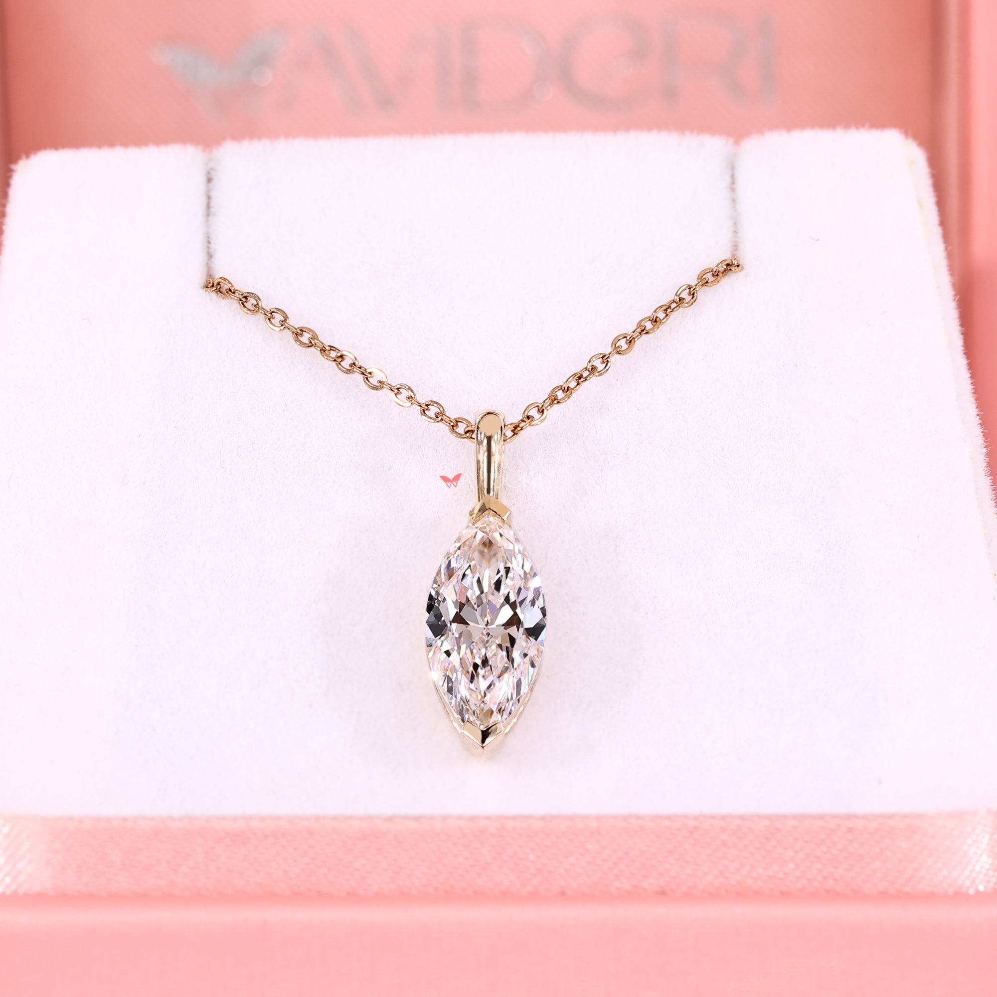 Gold necklace with a clear pendant on a pink and white background, featuring the brand 'Avidori'.