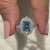 Blue Diamond Ring Held Between Two Finger.