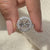 Prong set engagement ring with round diamond halo and pave band.
