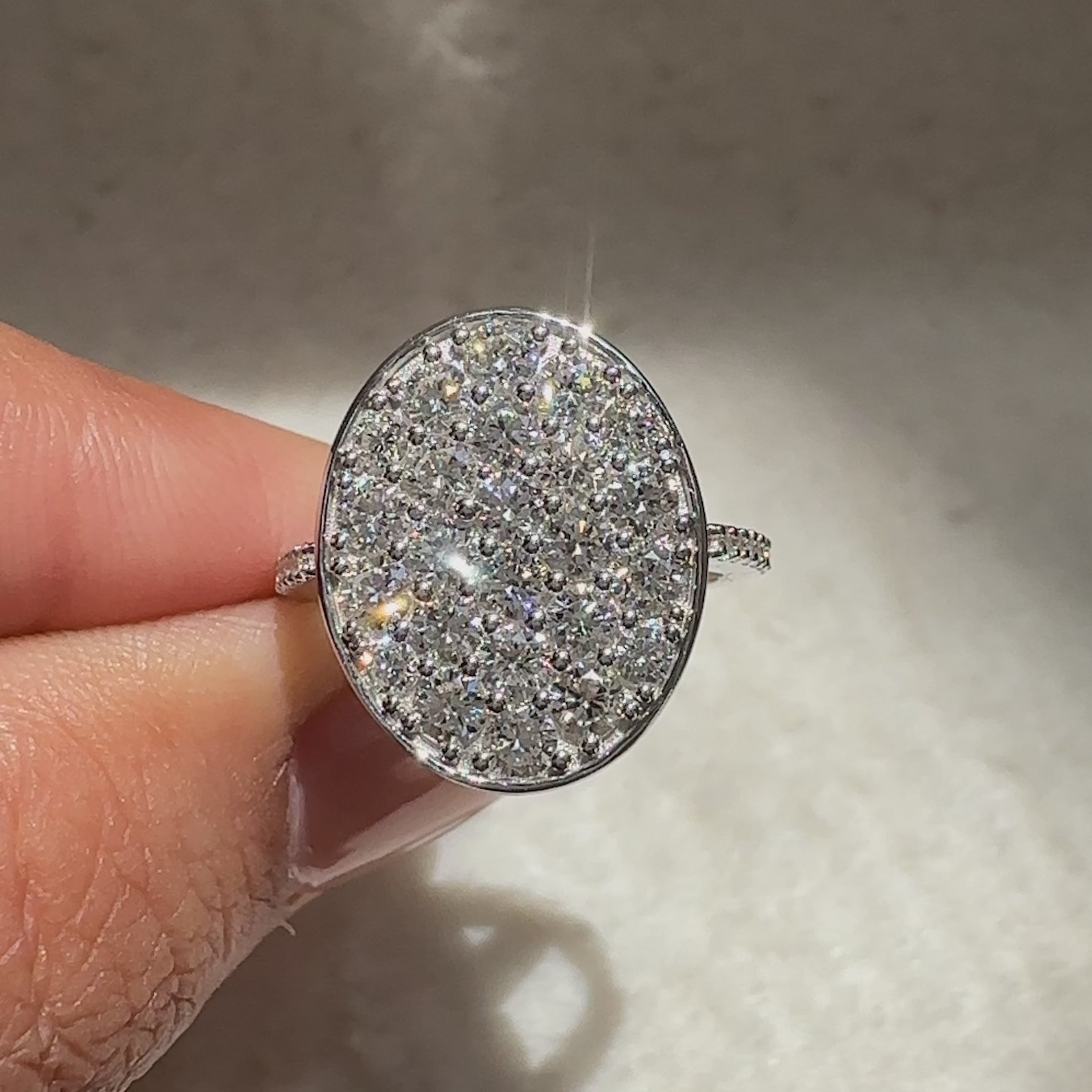 Cluster style round diamond ring with oval shape outline.
