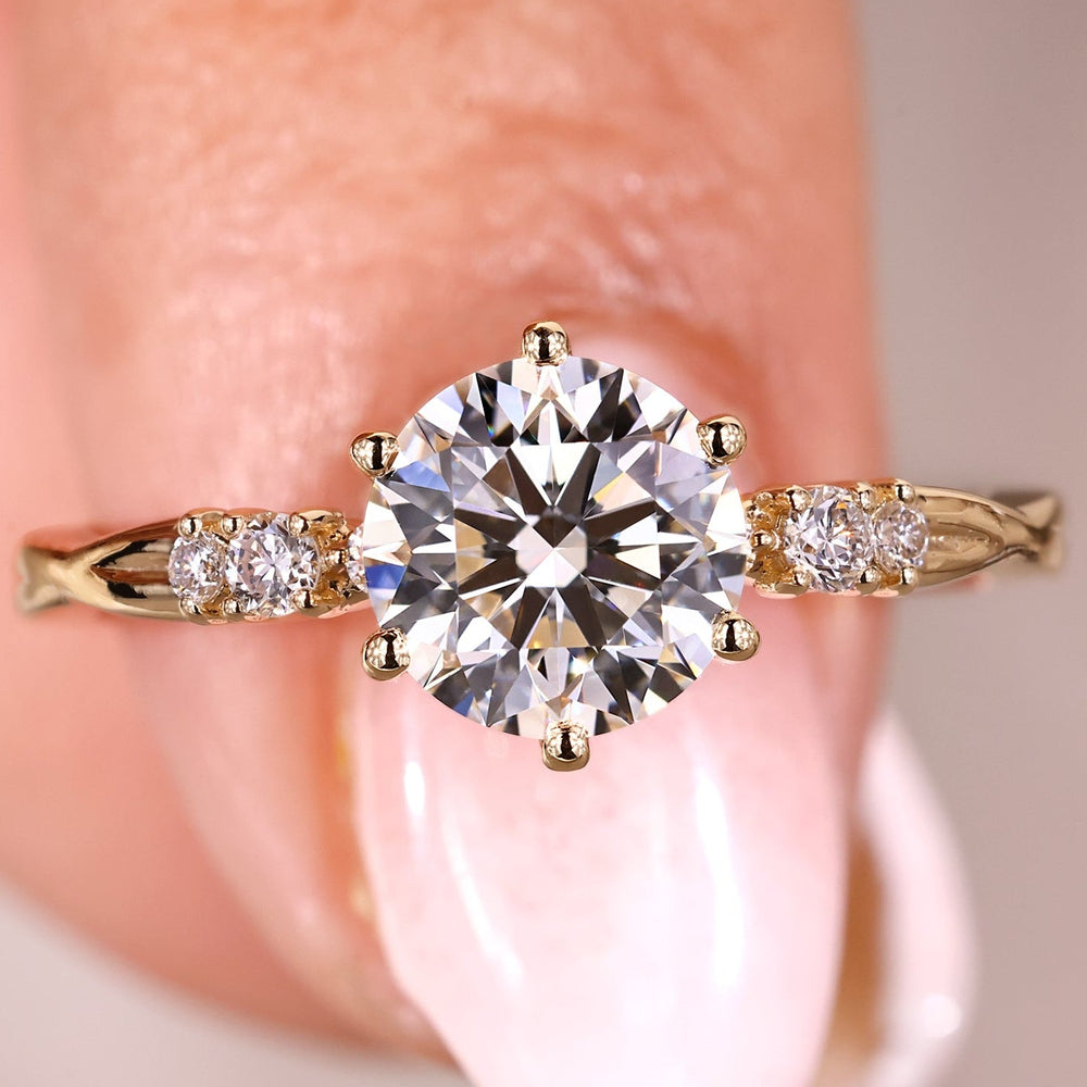 An image of a round diamond engagement ring set with six prongs, featuring a yellow gold band with sparkling side stones.