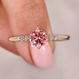 Pink diamond ring with round cut side stones in yellow gold.